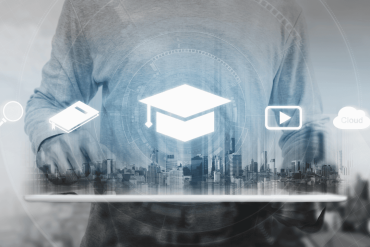 Persona, kas izmanto planšetdatoru ar digitālajām ikonām - cepurīti, grāmatu, palielināmo stiklu, atskaņošanas pogu un mākoni -, kas simbolizē tiešsaistes izglītību un e-mācības.