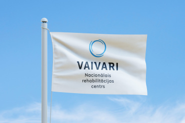 Zilā debesu fona priekšā, kurā redzami plāni mākoņi, plīvo balts karogs ar zilu apaļu logotipu un uzrakstu „VAIVARI Nacionālais rehabilitācijas centrs”.